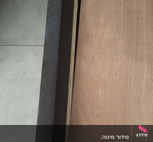 לוח עץ מונח על רצפה ליד קיר אפור
